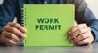 © J.G Studio - Person holding a green notebook with the words work permit written on the front cover page