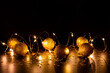 © Simplementbeau. - Guirlande lumineuse scintillante avec boules de Noël dorées à paillettes, posées sur un  fond brun foncé avec des étoiles dorées brillantes