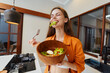 © SHOTPRIME STUDIO - Happy young woman enjoying healthy salad in modern kitchen, wearing casual orange outfit, showcasing fresh ingredients and vibrant colors