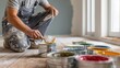 © xartproduction - Man kneeling on floor, dipping paintbrush into vibrant paint during renovation.
