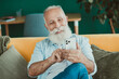 © deagreez - Senior man relaxed at home on sofa using smartphone smiling in a cozy living room setting