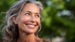 © วรรณภา มะโนศรี - Joyful mature woman with gray hair smiling warmly, enjoying nature, captured in bright light with a soft bokeh background of green foliage and a serene expression