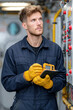 © NikonLamp - Male technician in blue coveralls using a digital multimeter in a control room with equipment