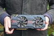 © FEDOR - One black modern hardware with two round coolers powerful electric graphic gaming video card for computer in man's hands in a brown jacket during daytime outdoors