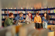 © Seventyfour - Group of multiethnic young adults sitting in library discussing ideas and taking notes, diverse men and women engaging in collaborative study session surrounded by bookshelves