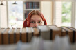 © Seventyfour - Portrait of Caucasian girl with red hair looking through bookshelf, eyes visible above row of books, standing in library or bookstore, natural light coming from window