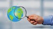 © AR Creations - Businessman holding a magnifying glass over a digital globe representing global analysis and research.