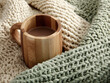 © Giggles - Warm wood mug staved cup hot coffee cozy blanket sage knit neutral yarn soft texture rustic style home comfort morning drink gently cradled by chunky knit, calming mood and tactile warmth