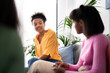 © Studio Marmellata - Three young women are engaged in a friendly conversation indoors. An African American woman in an orange shirt actively participates, sharing her thoughts with friends.
