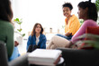 © Studio Marmellata - Diverse young women are gathered indoors, engaged in a friendly conversation. One woman smiles at the camera while others listen and interact, fostering connection.