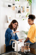© Studio Marmellata - Two young women share a friendly conversation in a bright, modern kitchen. One woman gestures while explaining something to her smiling friend, who sits on the counter