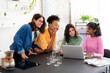 © Studio Marmellata - Four diverse young women gather around a laptop, collaborating and sharing ideas. They are smiling and engaged, working together at a table in a bright, modern setting.
