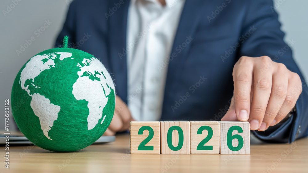 Businessman arranging wooden blocks with the year 2026 next to a green ...