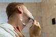 © Sarolta Nagy - Close-up view of a man shaving his face with a blue razor while applying shaving foam.