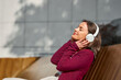© Sanja - Relaxed Woman Enjoying Music With White Headphones On Outdoor Bench In Sunlight