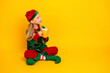 © deagreez - Adorable girl dressed as a festive elf in a vibrant costume sipping hot cocoa on a yellow background