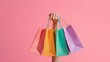 © nameera_hasan - hand holding colorful shopping bags pink background