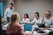 © qunica.com - A diverse group of professionals gathers around a conference table for a collaborative meeting. One member speaks on a mobile, another smiles, while laptops, documents, and coffee keep ideas flowing.