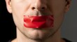 © MUHAMMAD - Portrait of young man with mouth covered by red tape symbolizing censorship, looking directly at camera, concept of silenced voices, freedom of speech and expression suppression