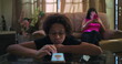 © Marco - Young Boy with curly hair lying on glass table scrolling smartphone, disengaged, while another young person sits on sofa in background on phone, themes of social media addiction and isolation