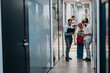 © qunica.com - A group of professionals stands in a glass-walled office corridor, examining folders and devices, collaborating on a project.
