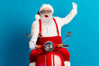 © deagreez - Santa on a bright red scooter waves hello in a festive Christmas scene against a blue background
