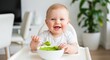 © Irina Tch - Happy baby eating green puree in a high chair, smiling at the camera