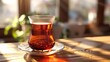 © RanaMuhammad - A clear glass of dark tea on a decorative saucer sitting on a wooden table near a bright window