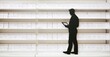 © antishock - Silhouette stands before shelves filled with boxes. Person uses tablet, reviewing items. Bright lighting, minimalist aesthetic.