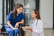 © PRIME STOCK LAB - Young female patient in wheelchair and female doctor discussing treatment plan with clipboard, caring consultation and hopeful expression