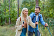 © Lumos sp - Hiking couple, young man and woman enjoys nature with trekking poles in a lush forest during a sunny day