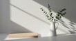© A R - Minimalist interior design with a white ceramic vase containing eucalyptus branches and a wooden board bathed in natural sunlight and shadow patterns on a white surface