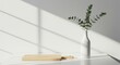 © A R - Minimalist interior with natural light and sharp shadows on a white surface, featuring a modern vase with eucalyptus leaves and a wooden cutting board