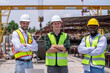 © APchanel - Engineers wearing safety helmets and reflective vests working construction site large overhead crane operation ensure efficient secure handling of heavy materials industrial engineering project.