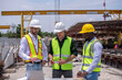 © APchanel - Engineers wearing safety helmets and reflective vests working construction site large overhead crane operation ensure efficient secure handling of heavy materials industrial engineering project.