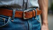 © Pete - Close up photo shows brown leather belt with silver buckle. Blue jeans and striped shirt. Fashion accessory for man. Details of outfit showing style and quality. Trendy casual look.