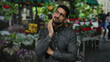 © Krakenimages.com - Young man in a thoughtful pose at a vibrant flower shop with colorful blooms, creating an outdoor setting filled with life and beauty, wearing casual attire with a contemplating expression.