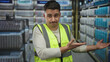 © Krakenimages.com - Young hispanic man wearing a reflective vest points skeptically indoors on a cruise boat with a seaside view alongside stacked packages.