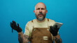 © Krakenimages.com - Man with beard wearing gloves holding notebook against blue background looking thoughtful and curious in casual outfit with tattoos visible while isolated.