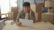© Krakenimages.com - Young man in a new home talking on the phone, examining documents with moving boxes around in a bright living room setting.