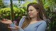 © Krakenimages.com - Young caucasian woman waves hand for dismissal and scrunches face in green park amid tropical foliage; disgust.