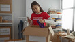 © Krakenimages.com - Woman volunteering in charity center wearing red shirt organizing donations indoors using phone surroundings with boxes.