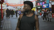 © Krakenimages.com - Man smiling and looking to the side with bare arms in a crowded city street market, wearing black tank top amid blurred shoppers and stalls; urban confidence.