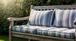 © Anna - A rustic wooden bench with striped cushions in a sunny garden. Comfortable outdoor furniture for backyard relaxation