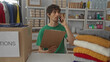 © Krakenimages.com - Man holds clipboard and talks on phone inside a building donation center amid stacked clothes and boxes on shelves; compassion.