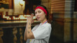 © Krakenimages.com - Woman in church with tattoos wearing medal and headband points finger guns playfully, blending athletic and spiritual themes in a unique indoor setting with candles.