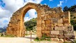 © Telo - Majestic stone archway, partially intact, stands against a bright blue sky with scattered clouds. The ancient structure hints at history