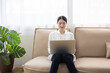 © hidez - Woman Sitting on Sofa Using Laptop in Bright Living Room