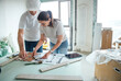 © Dasha Petrenko - Male construction worker and female architect collaborating on building plans at a table in a renovation site, showcasing teamwork and design process in a modern workspace