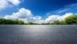 © Hallie - empty asphalt lot under a vibrant blue sky with fluffy clouds and green trees in the background